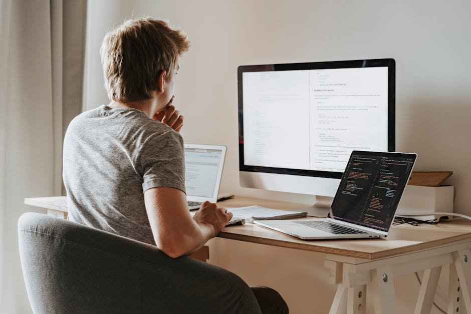 A man deeply engaged in software development with two laptops and a desktop monitor.