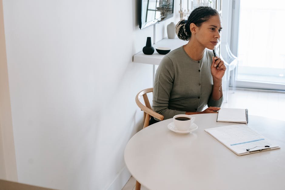 Concentrated ethnic female HR interviewer or psychologist in formal clothes sitting at round table with pen and notepad while looking away in contemplation