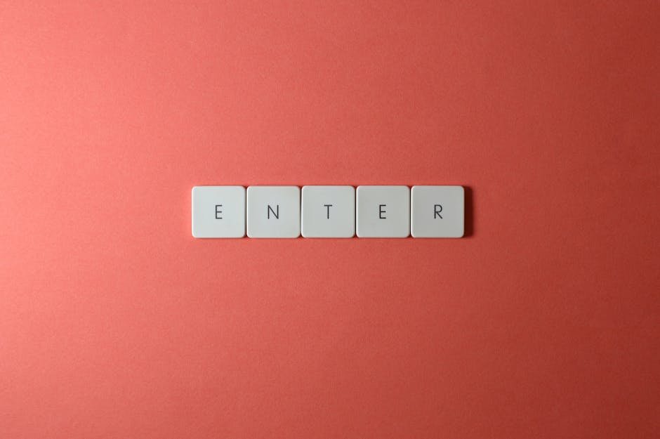 Close-up of five keyboard letter tiles spelling 'ENTER', placed on a coral backdrop.