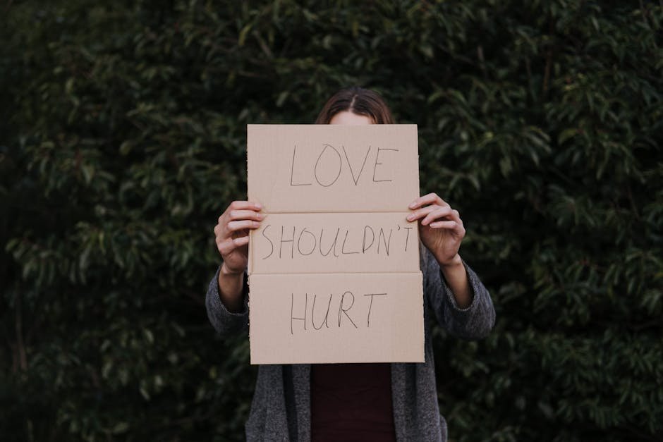 Person holding a sign reading 'LOVE SHOULDN'T HURT' in a protest against domestic violence.