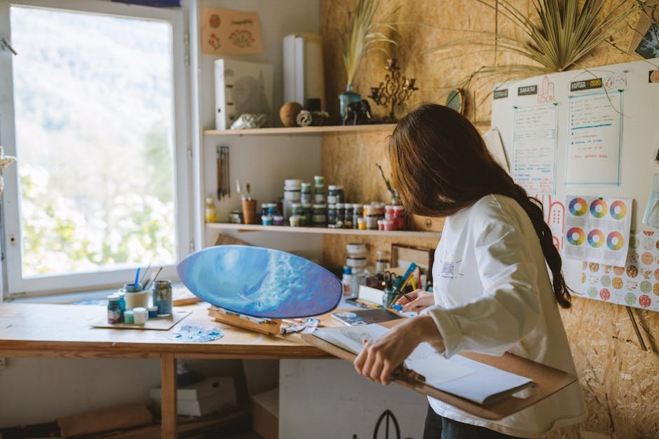 Woman artist painting a blue ocean scene on a skateboard in a cozy art studio.