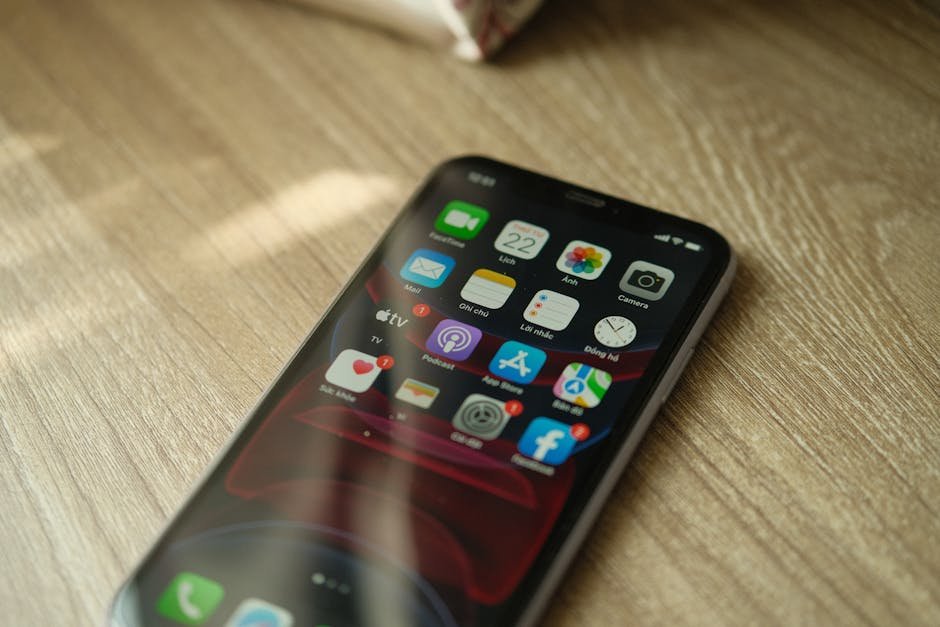 A close-up view of a smartphone displaying various apps on a wooden surface.