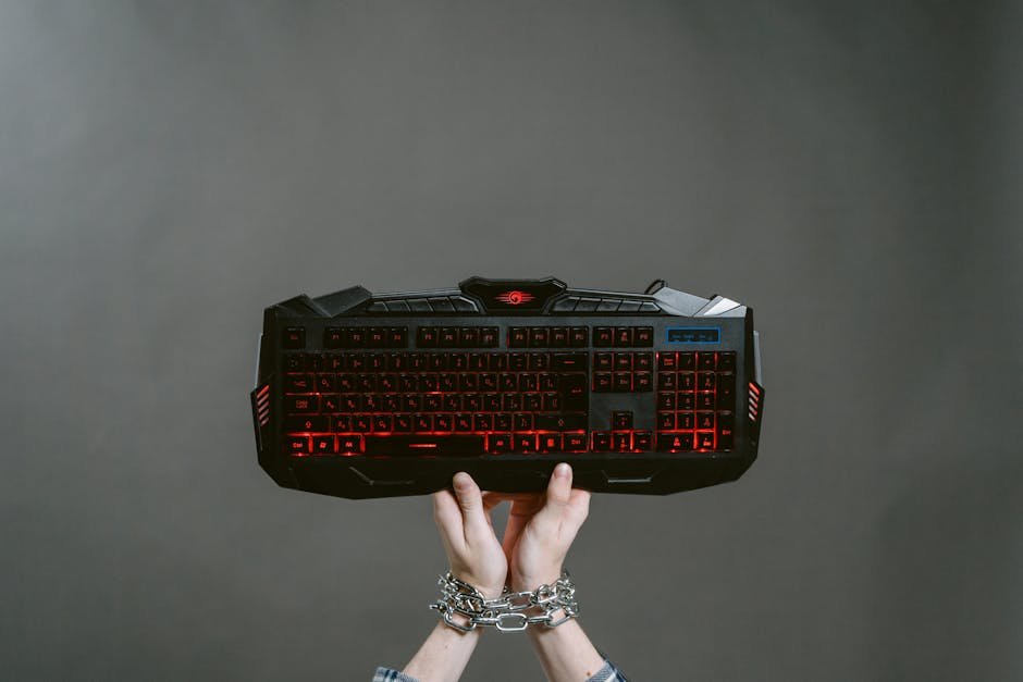 Hands bound by chains holding a mechanical gaming keyboard with red backlight.
