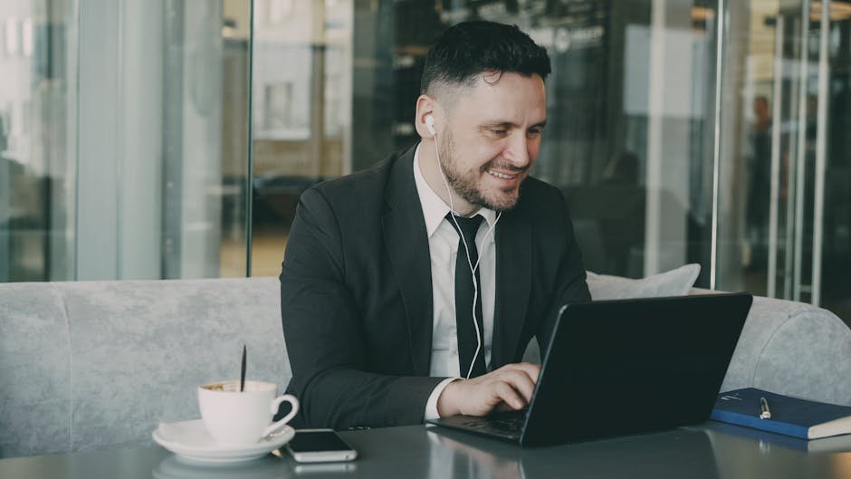 Businessman in a suit using a laptop in a cafe, enjoying coffee and listening to headphones.
